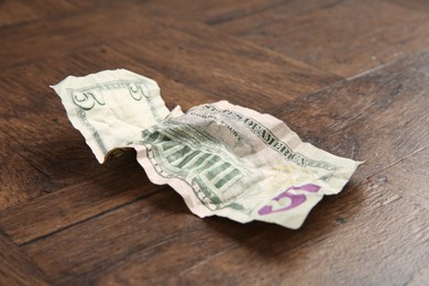 Photo of One crumpled dollar banknote on wooden table, closeup