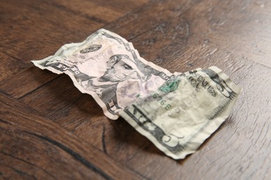 Photo of One crumpled dollar banknote on wooden table, closeup