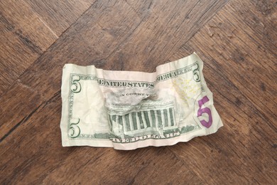 Photo of One crumpled dollar banknote on wooden table, top view