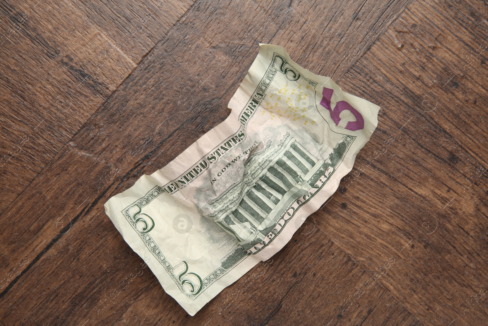 Photo of One crumpled dollar banknote on wooden table, top view