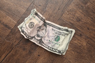 Photo of One crumpled dollar banknote on wooden table, top view