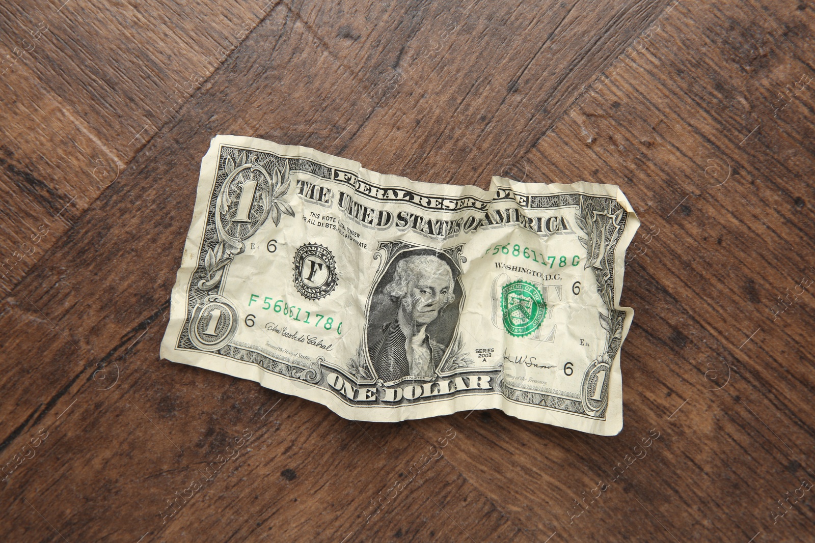 Photo of One crumpled dollar banknote on wooden table, top view