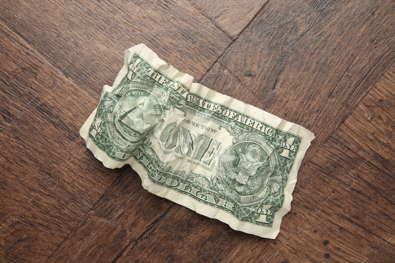 Photo of One crumpled dollar banknote on wooden table, top view