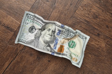 Photo of One crumpled dollar banknote on wooden table, top view