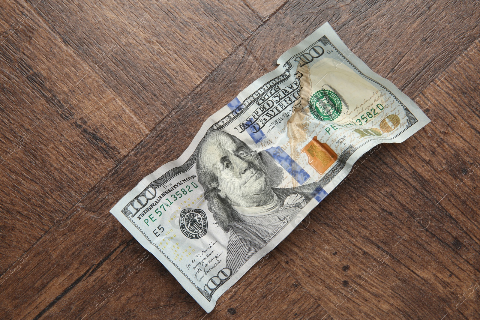 Photo of One crumpled dollar banknote on wooden table, top view