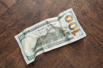 Photo of One crumpled dollar banknote on wooden table, top view