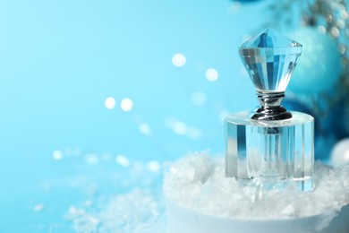 Photo of Christmas composition with perfume bottle and snow on light blue background, closeup. Space for text