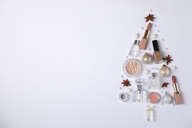 Christmas tree shape made of perfume bottles and cosmetic products on white background, flat lay. Space for text