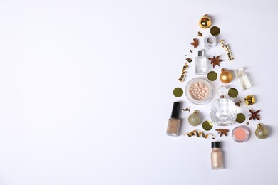 Photo of Christmas tree shape made of perfume bottles and cosmetic products on white background, flat lay. Space for text