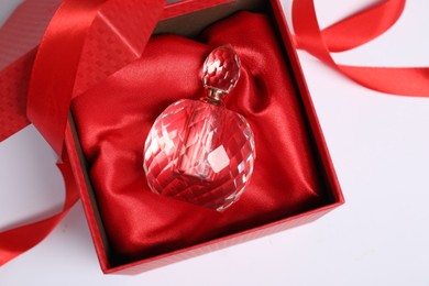 Photo of Christmas gift. Perfume bottle in red box and ribbon on white background, top view