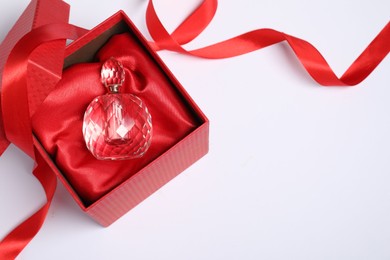 Christmas gift. Perfume bottle in red box and ribbon on white background, top view. Space for text