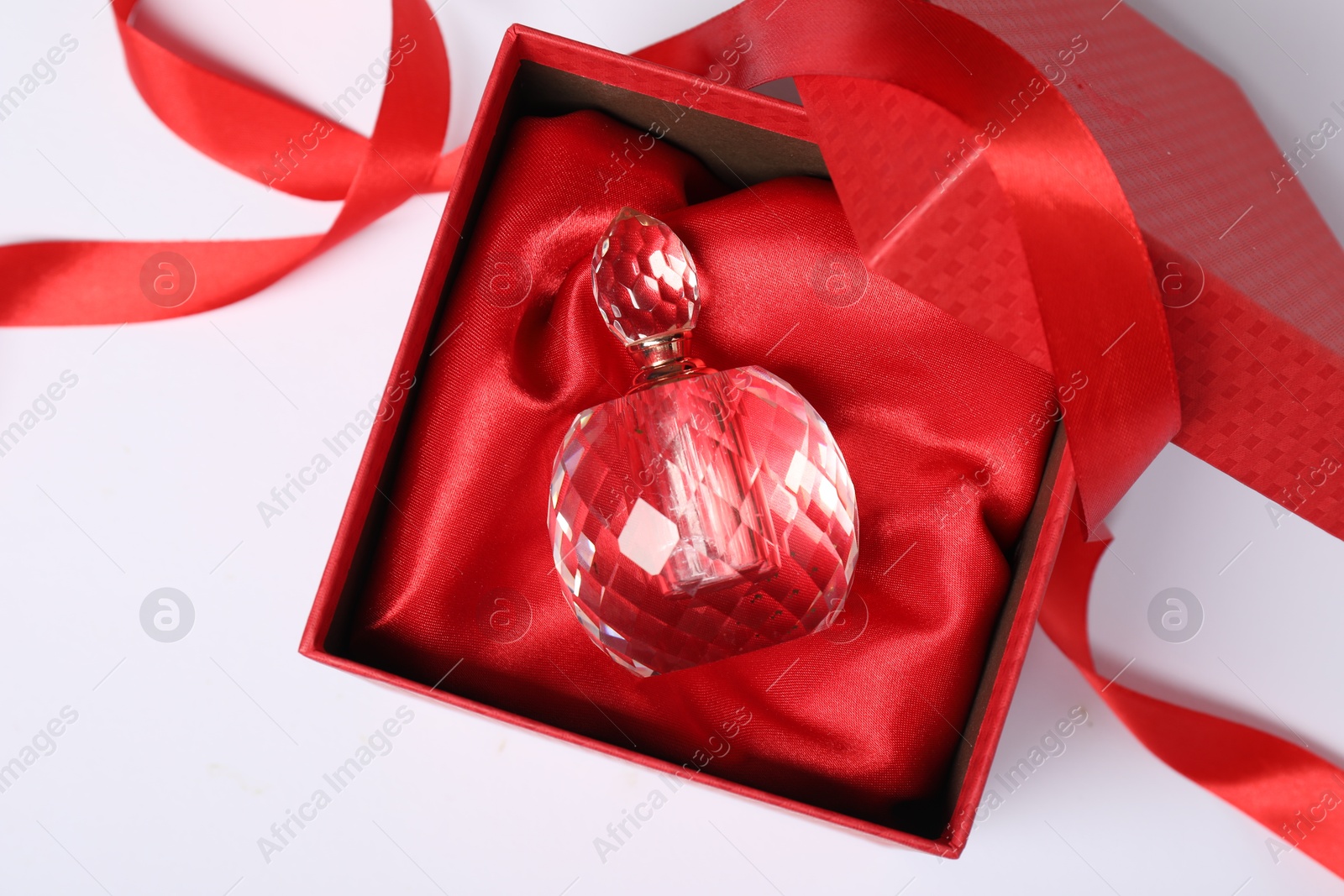 Photo of Christmas gift. Perfume bottle in red box and ribbon on white background, top view