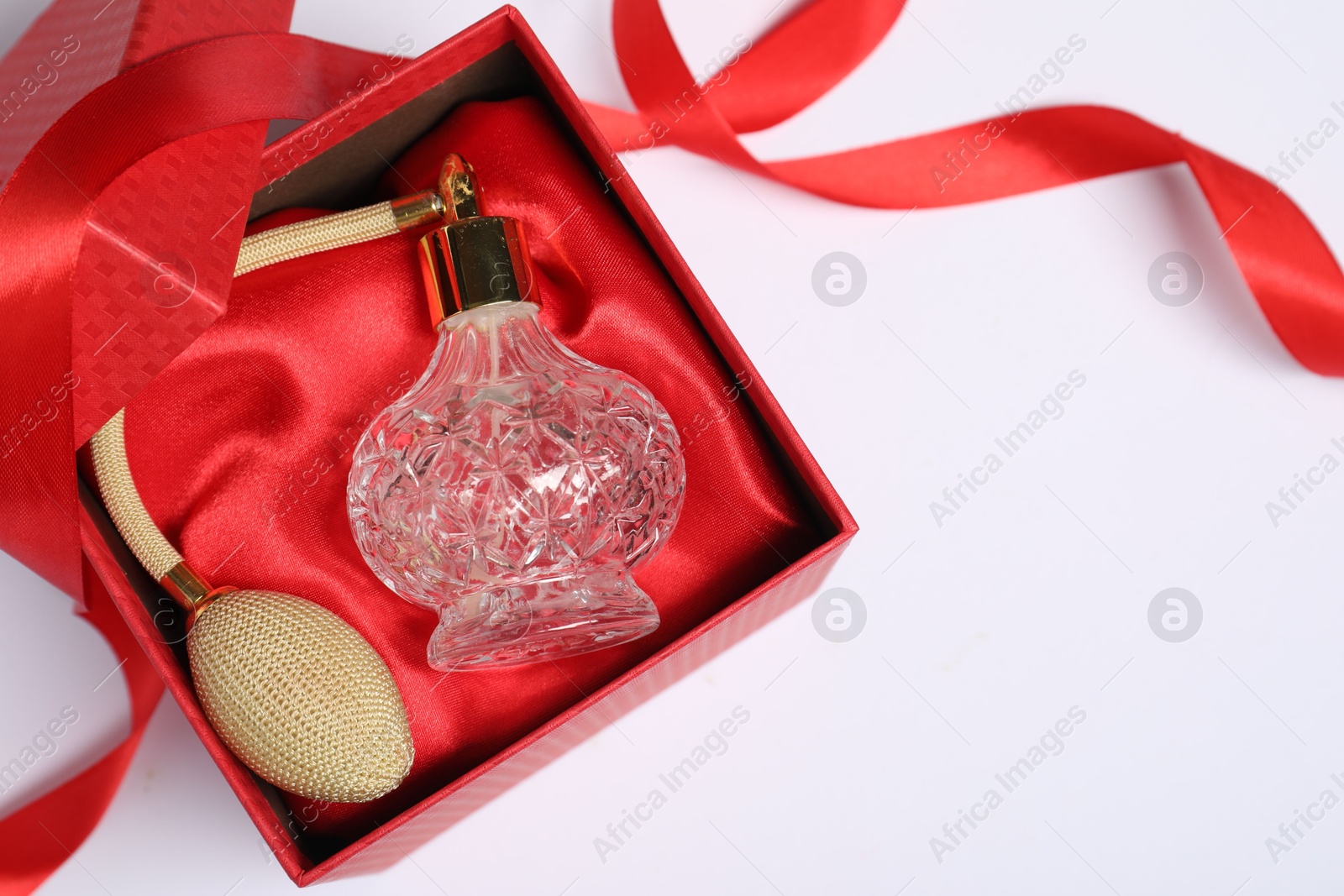 Photo of Christmas gift. Perfume bottle in red box and ribbon on white background, top view. Space for text