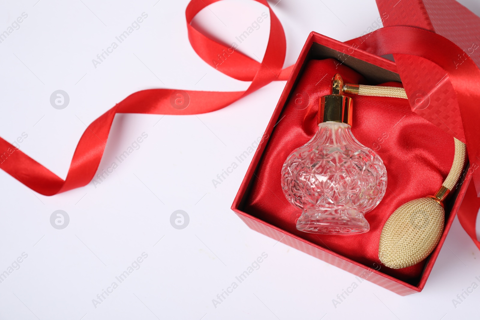 Photo of Christmas gift. Perfume bottle in red box and ribbon on white background, top view. Space for text