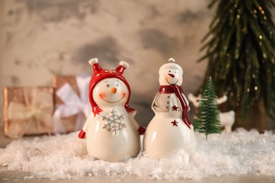 Photo of Funny snowmen figures and artificial snow on table, closeup