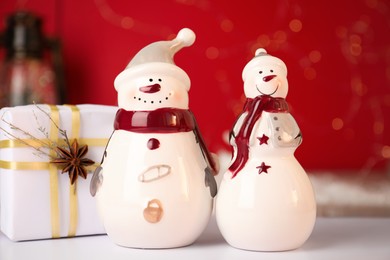 Photo of Funny snowmen figures and Christmas gift on white table, closeup