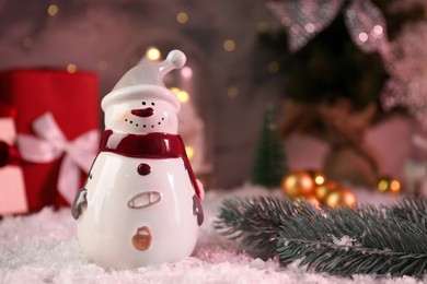 Photo of Funny snowman figure and fir branch on artificial snow, closeup