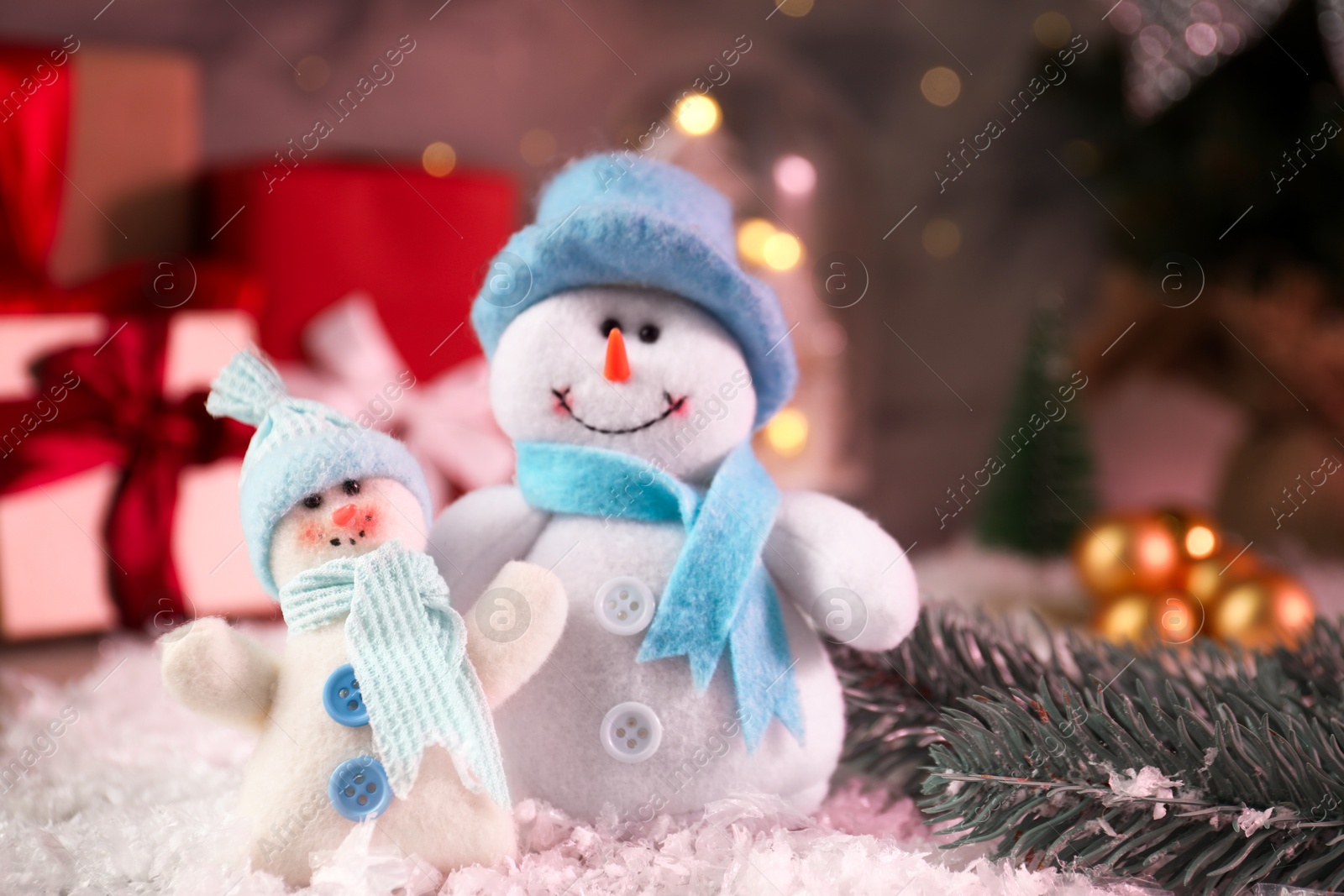 Photo of Funny snowmen figures and fir branch on artificial snow, closeup