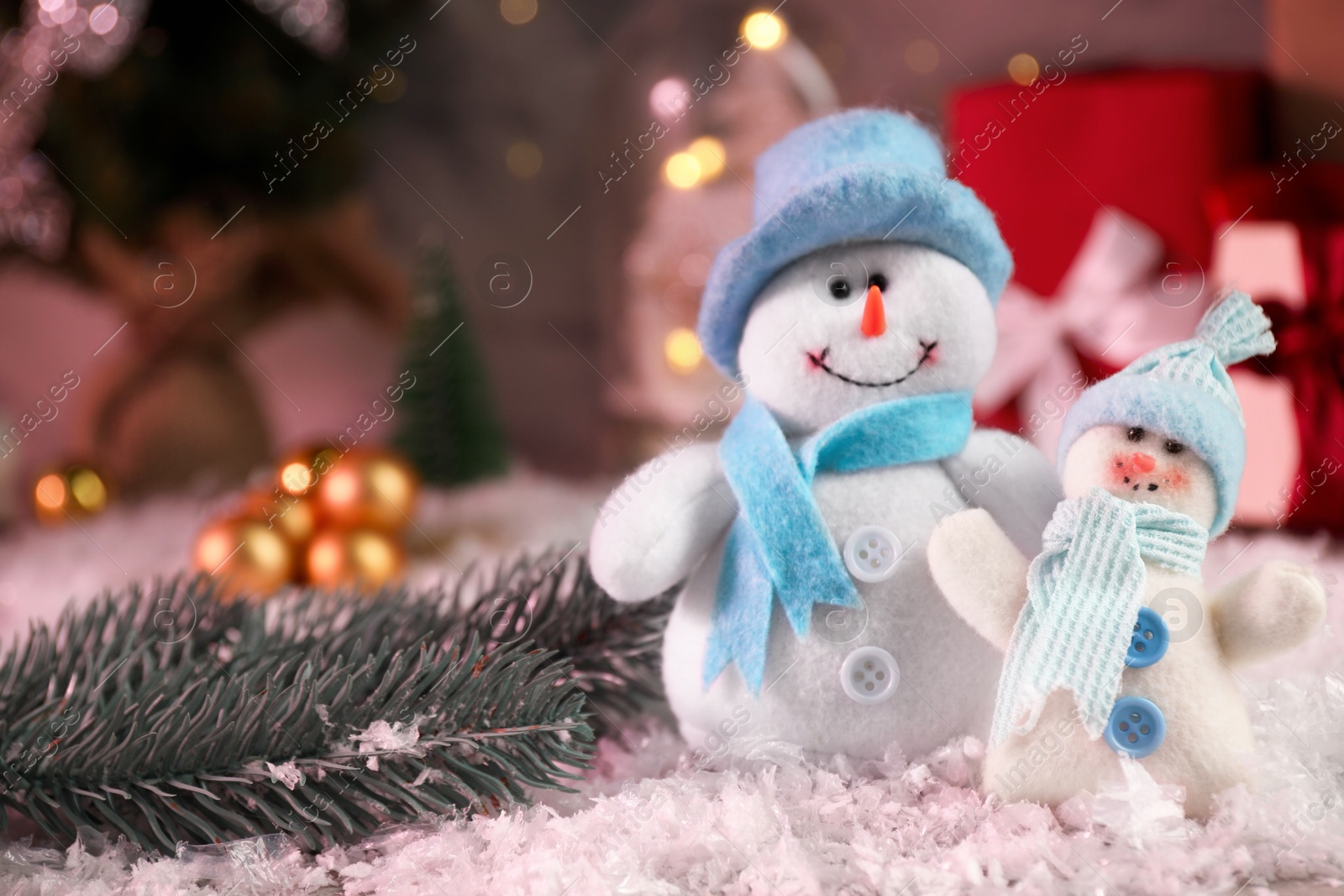 Photo of Funny snowmen figures and fir branch on artificial snow, closeup