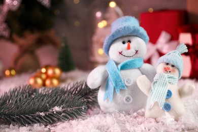 Photo of Funny snowmen figures and fir branch on artificial snow, closeup