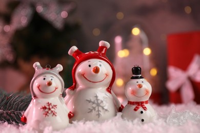 Photo of Funny snowmen figures and fir branch on artificial snow, closeup