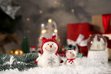 Photo of Funny snowmen figures and fir branch on artificial snow, closeup