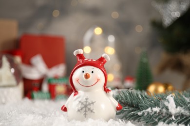 Photo of Funny snowman figure and fir branch on artificial snow, closeup