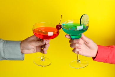 Photo of Friends with glasses of refreshing cocktails on yellow background, closeup