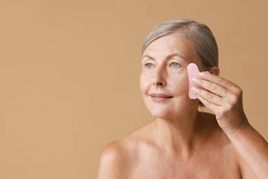 Photo of Beautiful woman doing facial massage with gua sha tool on beige background, space for text