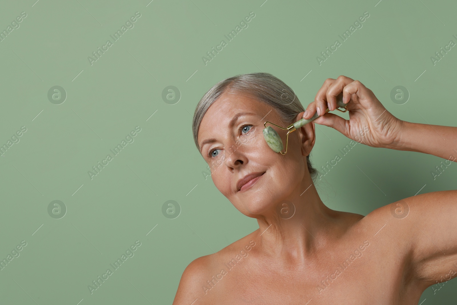 Photo of Beautiful woman doing facial massage with roller on light green background, space for text