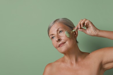 Beautiful woman doing facial massage with roller on light green background, space for text