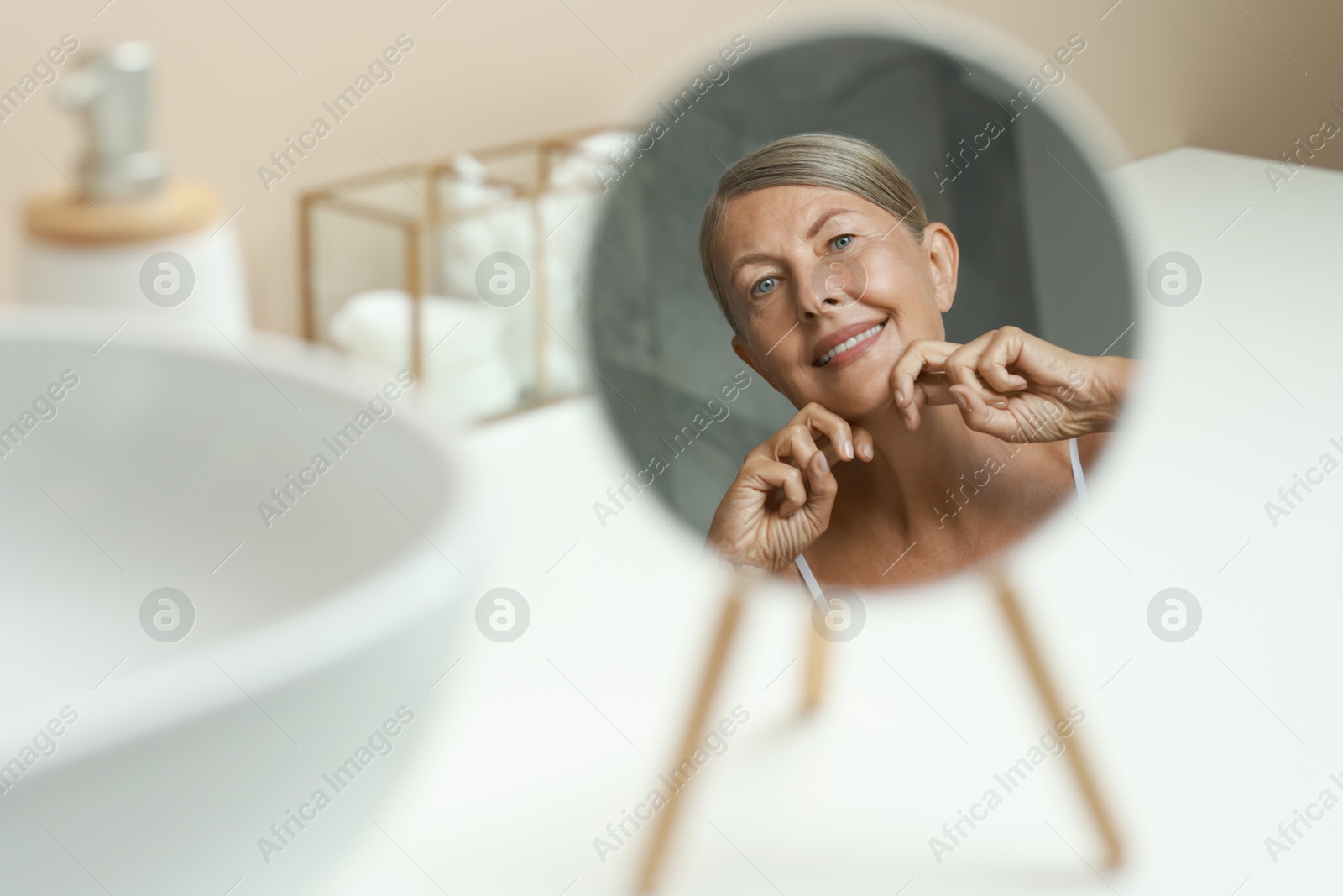 Photo of Beautiful woman doing facial massage near mirror at home