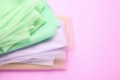 Folded tulle fabrics of different colors on pink background, top view. Space for text