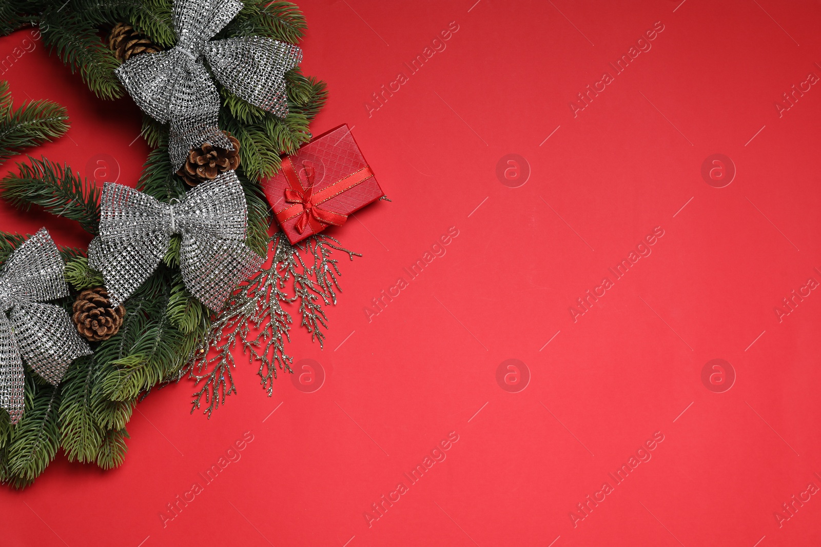 Photo of Christmas wreath with cones, gift box and bows on red table, flat lay. Space for text