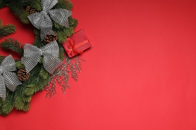 Photo of Christmas wreath with cones, gift box and bows on red table, flat lay. Space for text