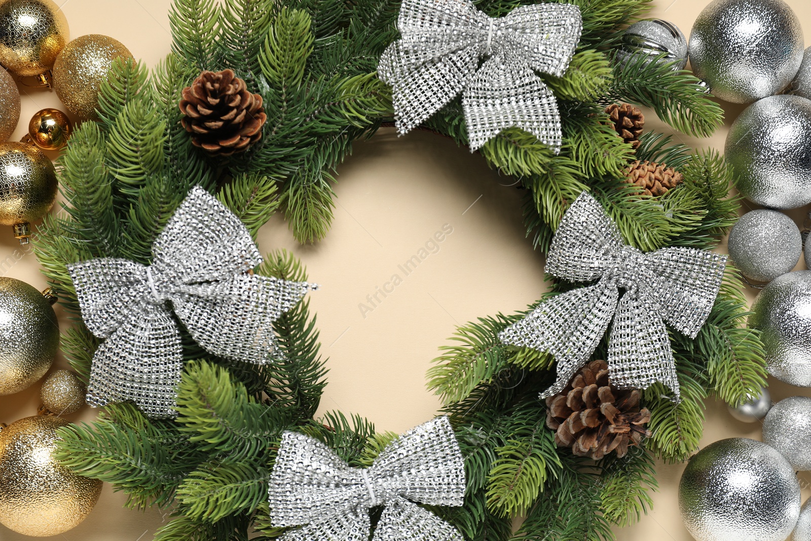 Photo of Christmas wreath with cones, bows and baubles on beige background, flat lay