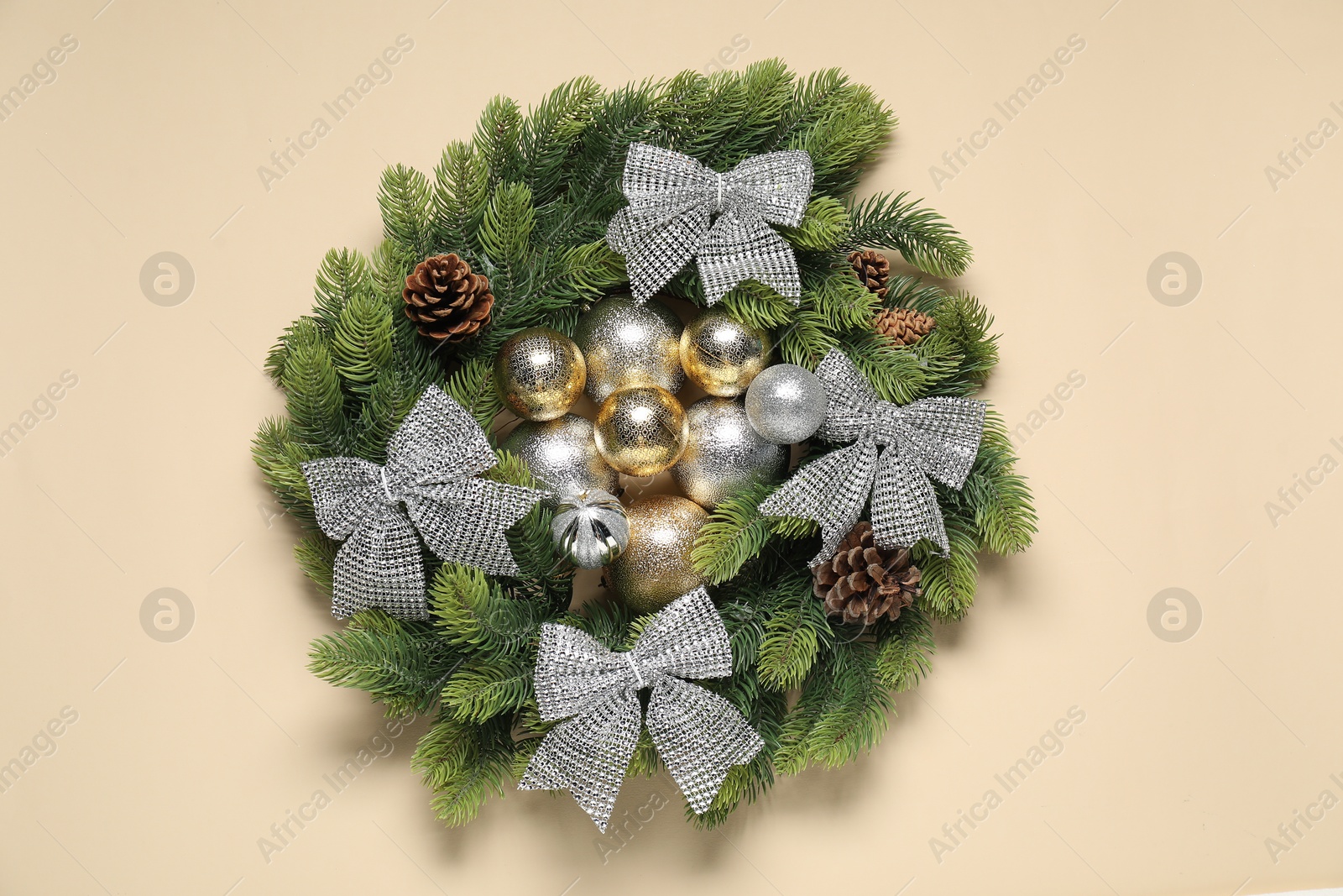 Photo of Christmas wreath with cones, bows and baubles on beige background, top view