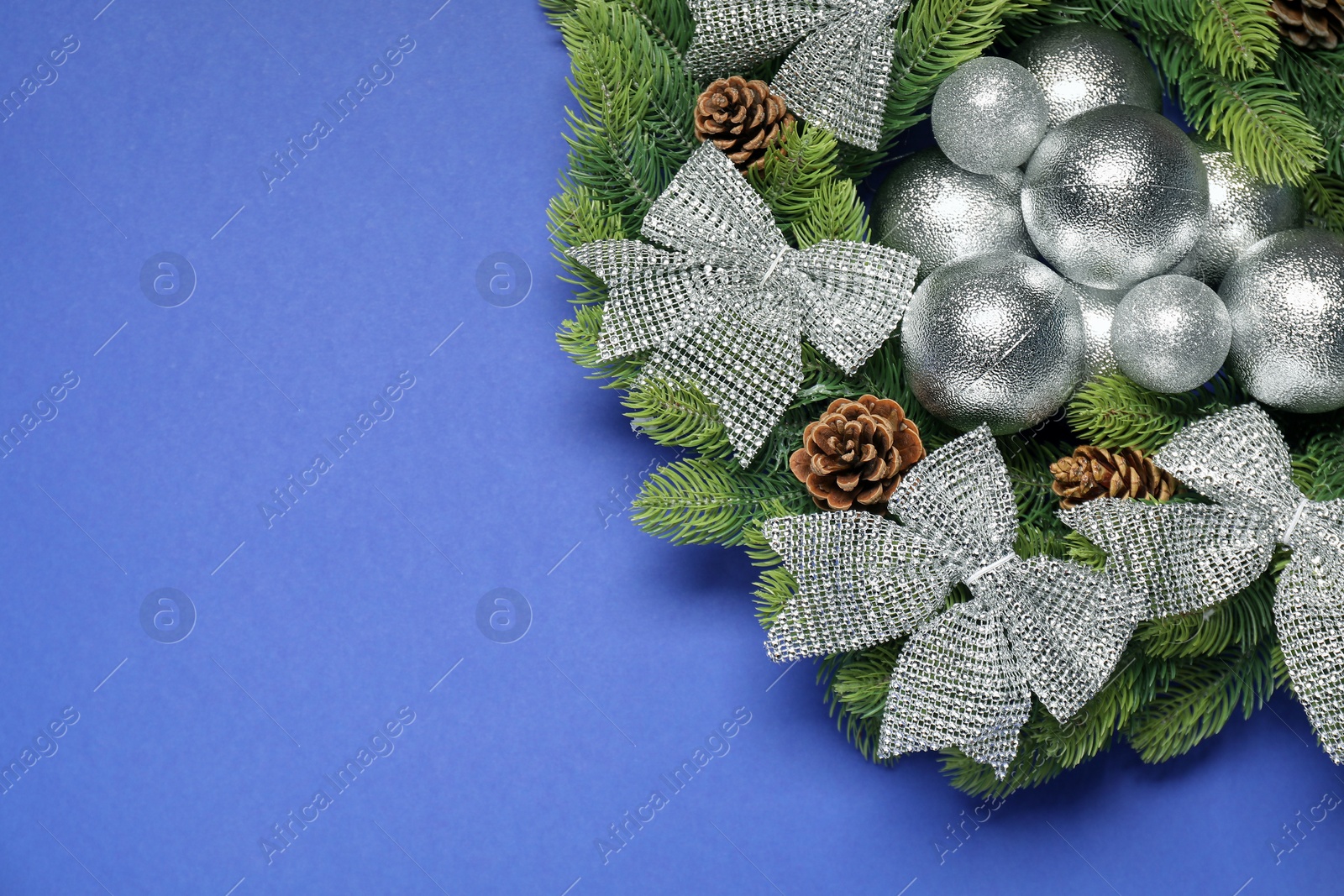 Photo of Christmas wreath with cones, bows and baubles on blue background, top view. Space for text