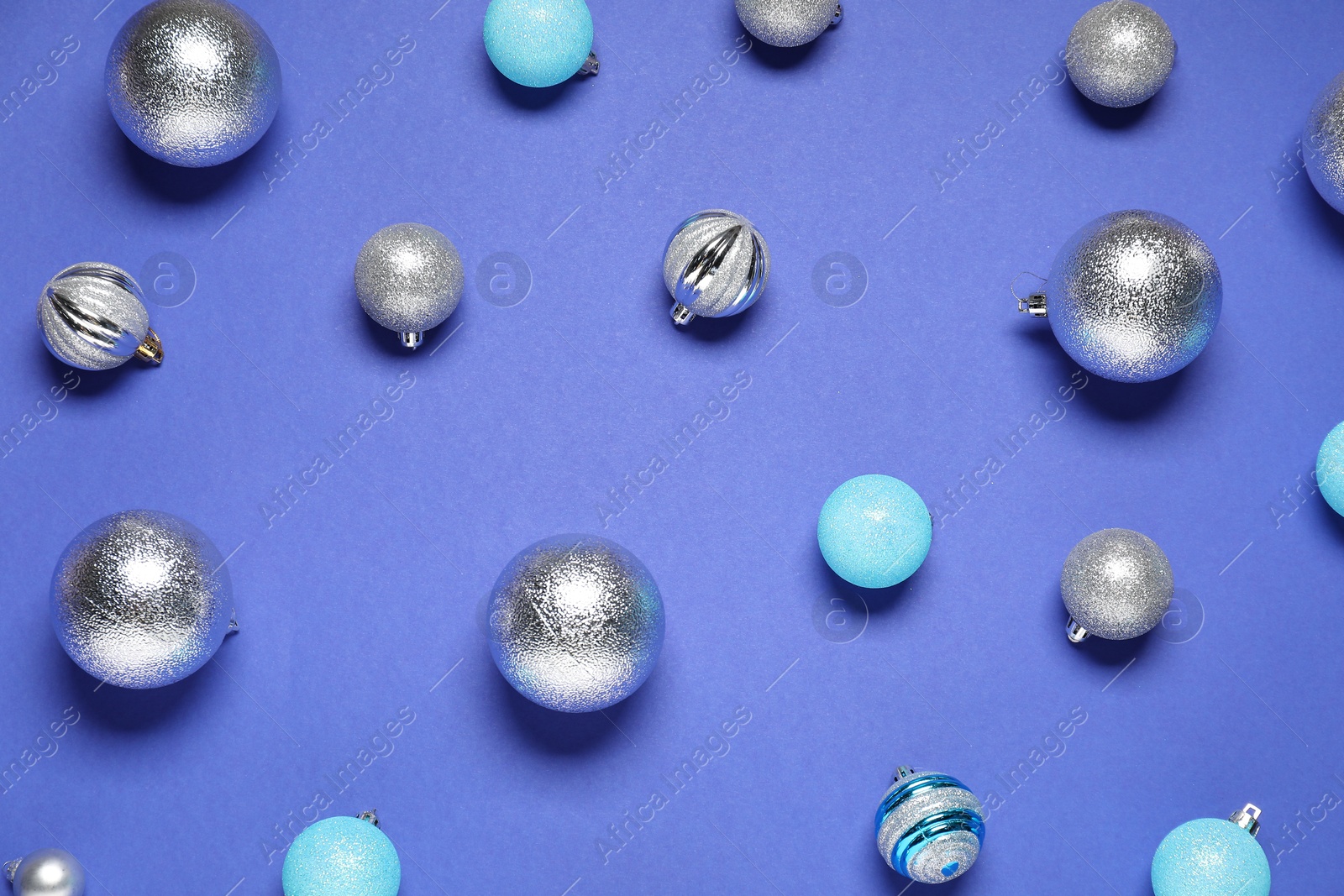 Photo of Different shiny baubles on blue background, flat lay