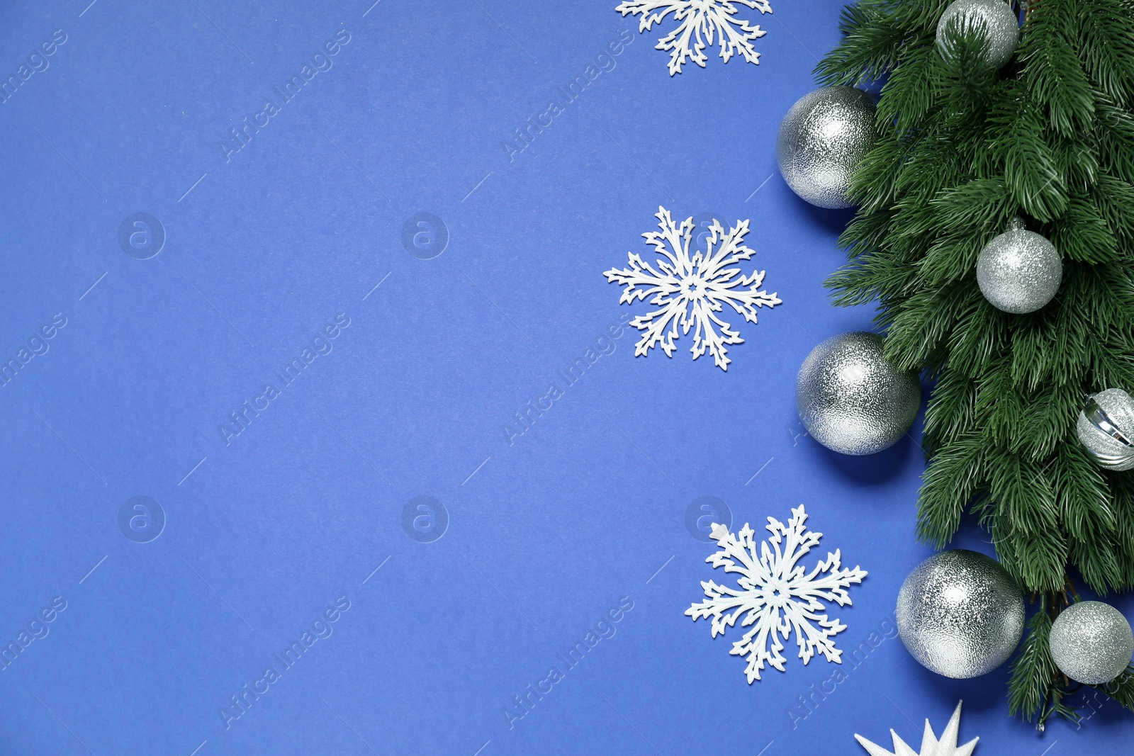 Photo of Fir tree branches, shiny baubles and decorative snowflakes on blue background, flat lay. Space for text