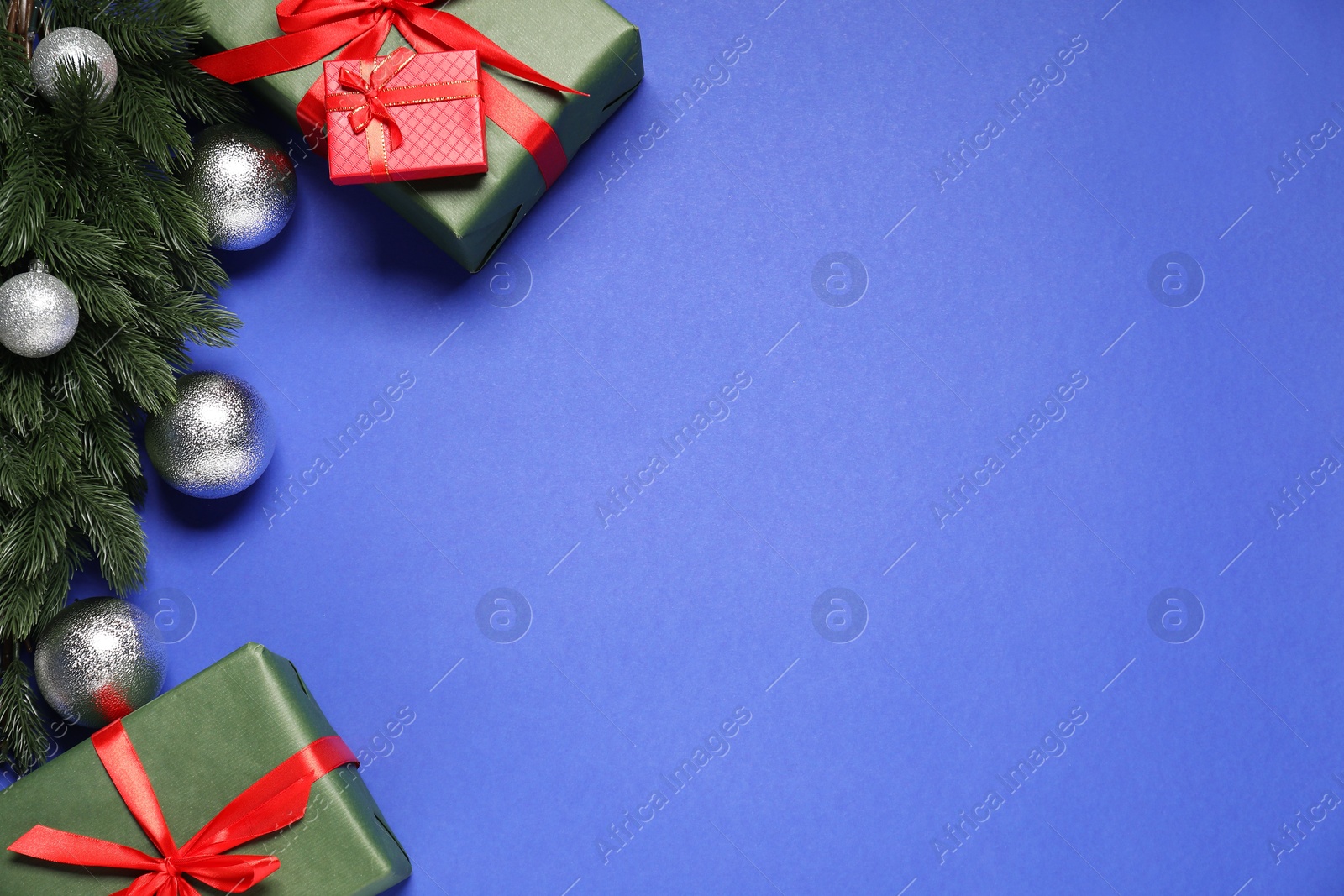 Photo of Fir tree branches, shiny baubles and gift boxes on blue background, flat lay. Space for text