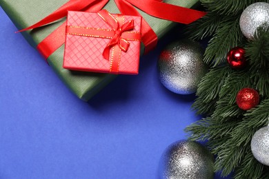 Photo of Fir tree branches, shiny baubles and gift boxes on blue background, flat lay. Space for text