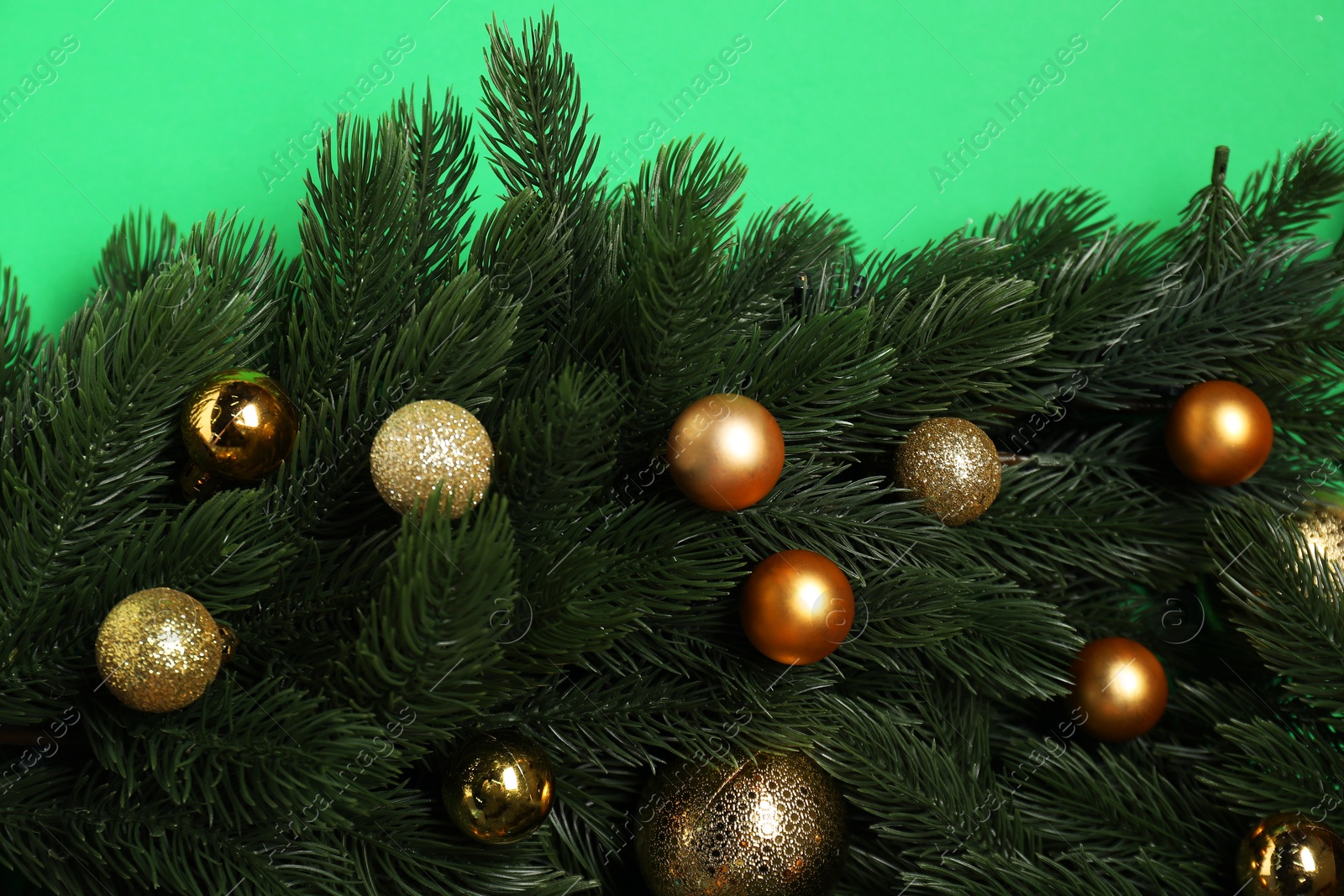 Photo of Fir tree branches and shiny baubles on green background, top view