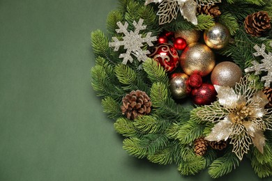 Photo of Christmas wreath with cones, baubles and decorative snowflakes on green background, top view. Space for text