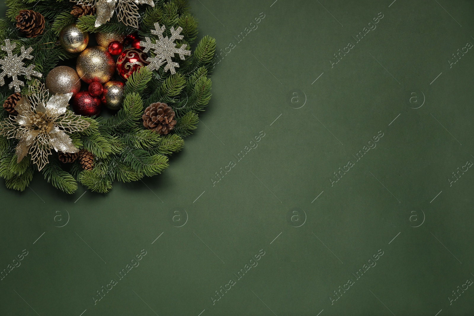 Photo of Christmas wreath with cones, baubles and decorative snowflakes on green background, top view. Space for text