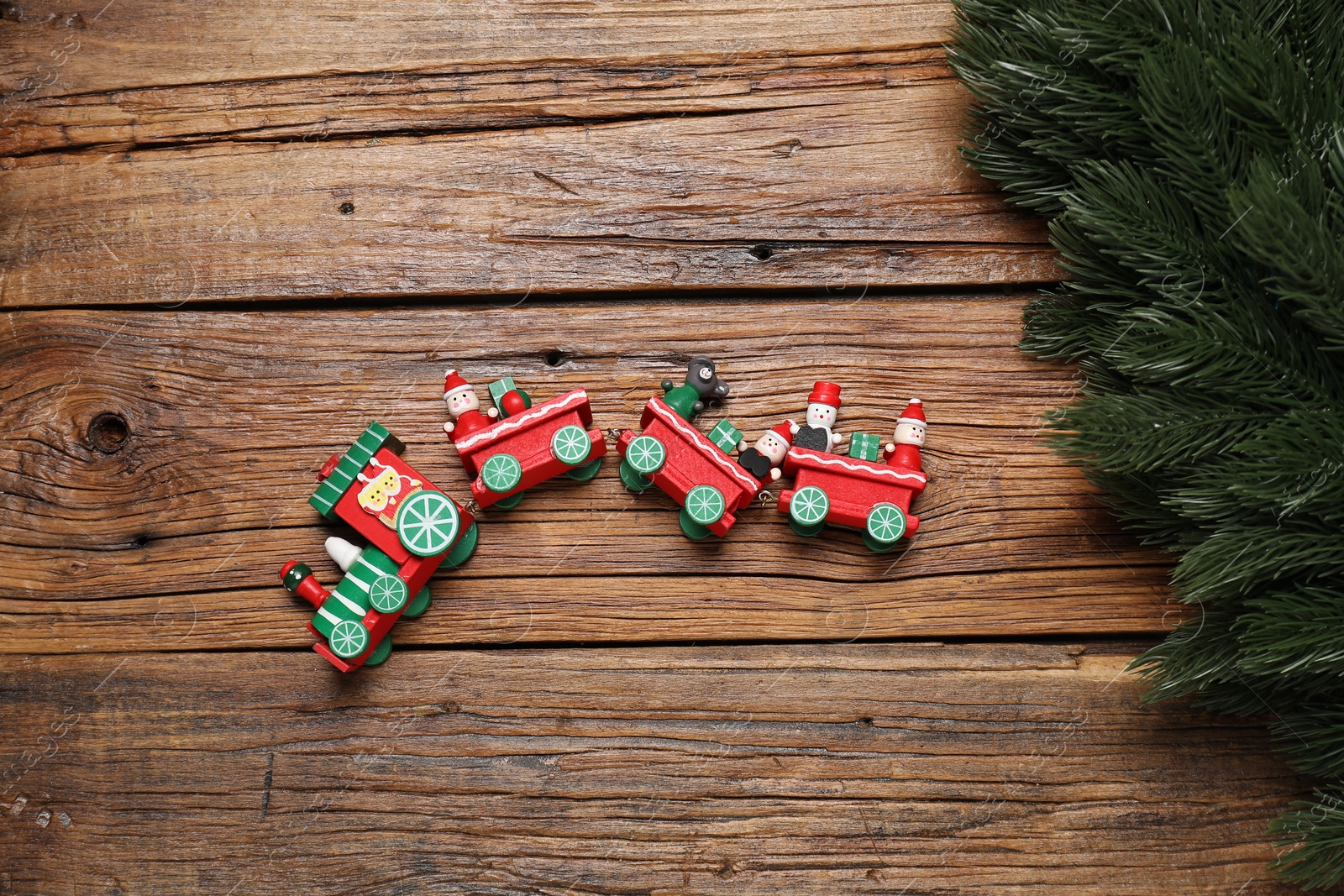 Photo of Toy train and fir tree branches on wooden table, flat lay