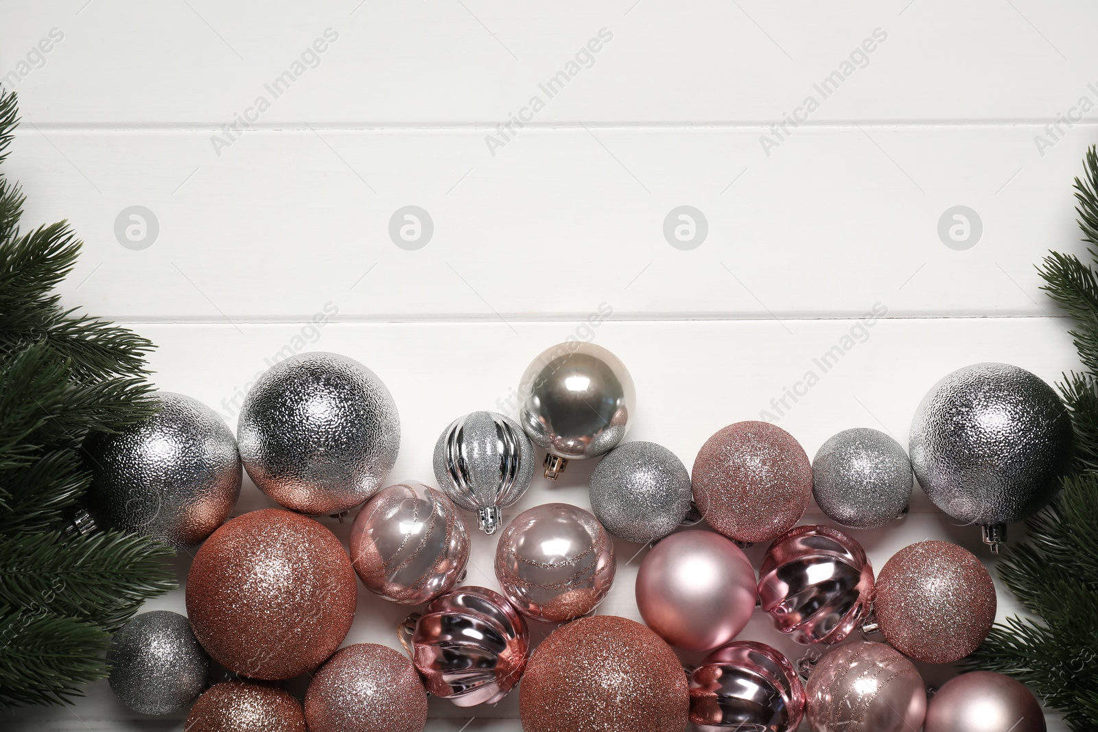 Photo of Fir tree branches and baubles on white wooden table, flat lay. Space for text