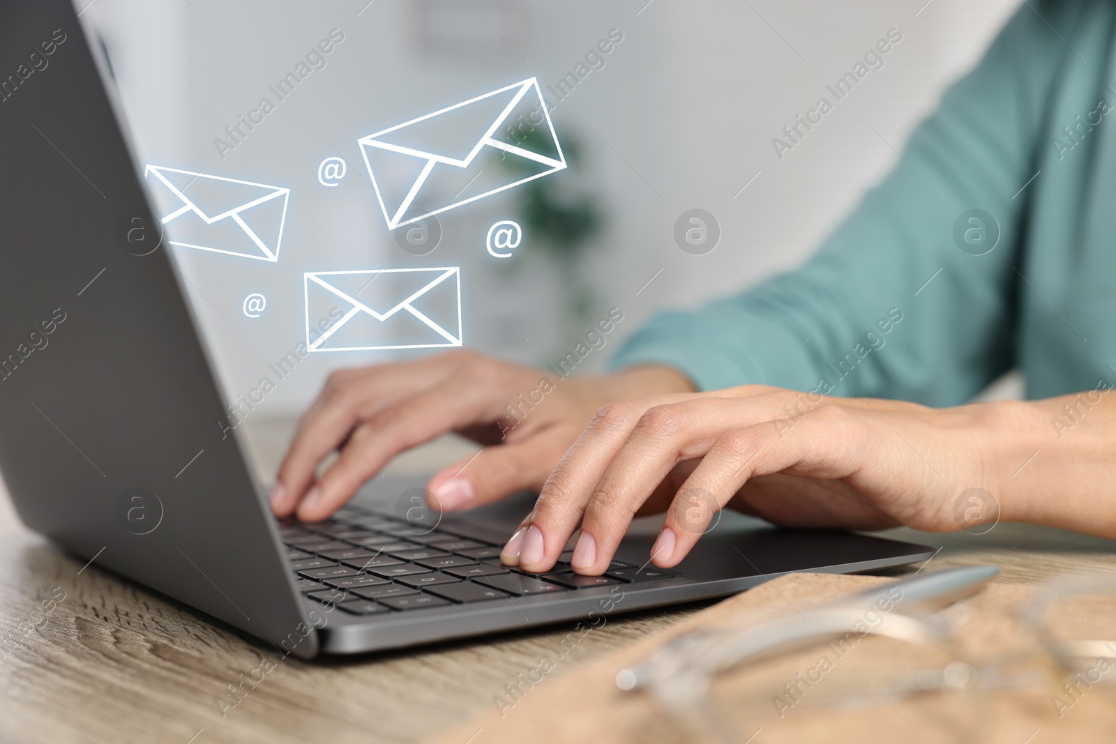 Image of Woman using laptop at table, closeup. E-mail address signs and envelopes over computer