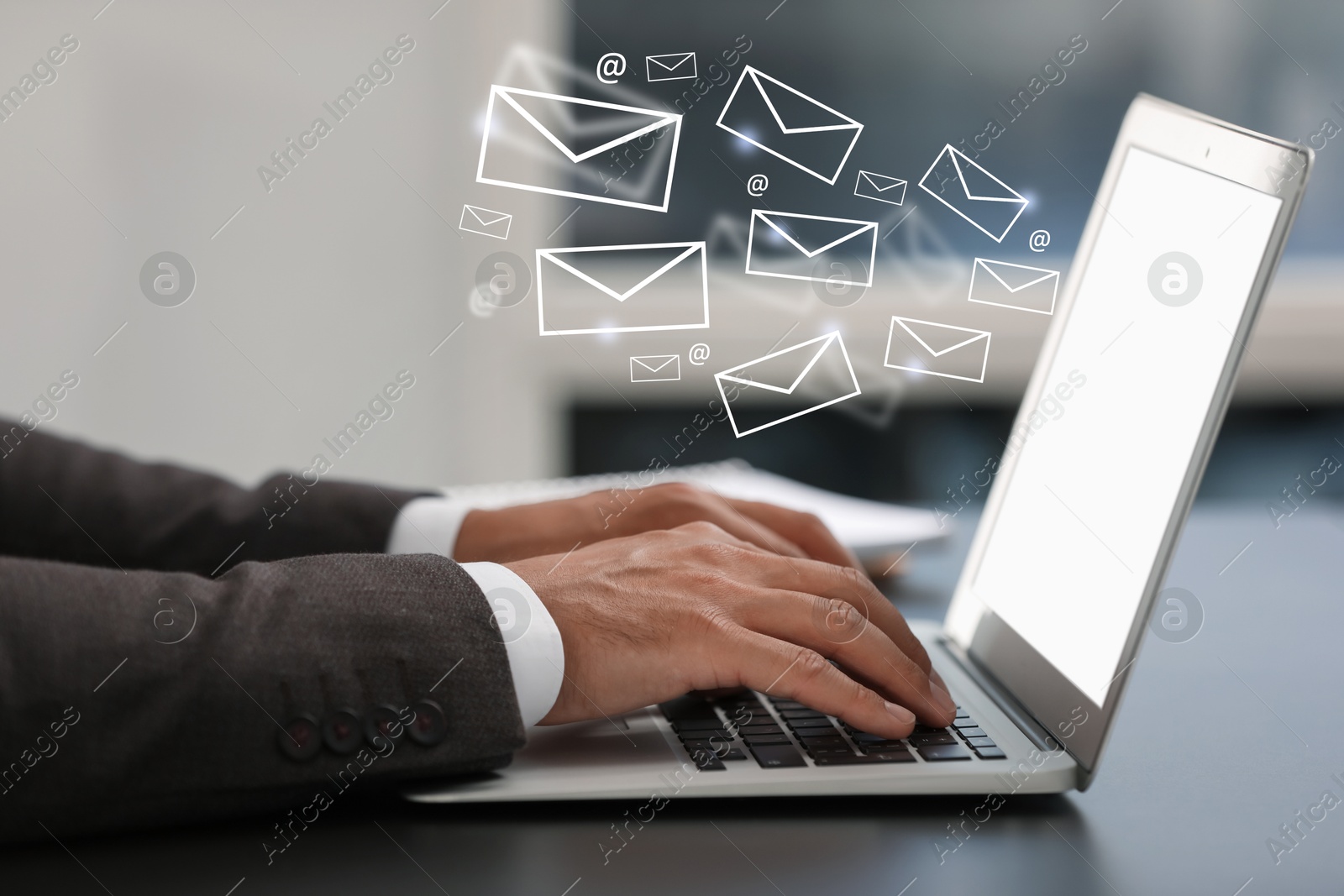 Image of Man using laptop at table, closeup. E-mail address signs and envelopes over computer