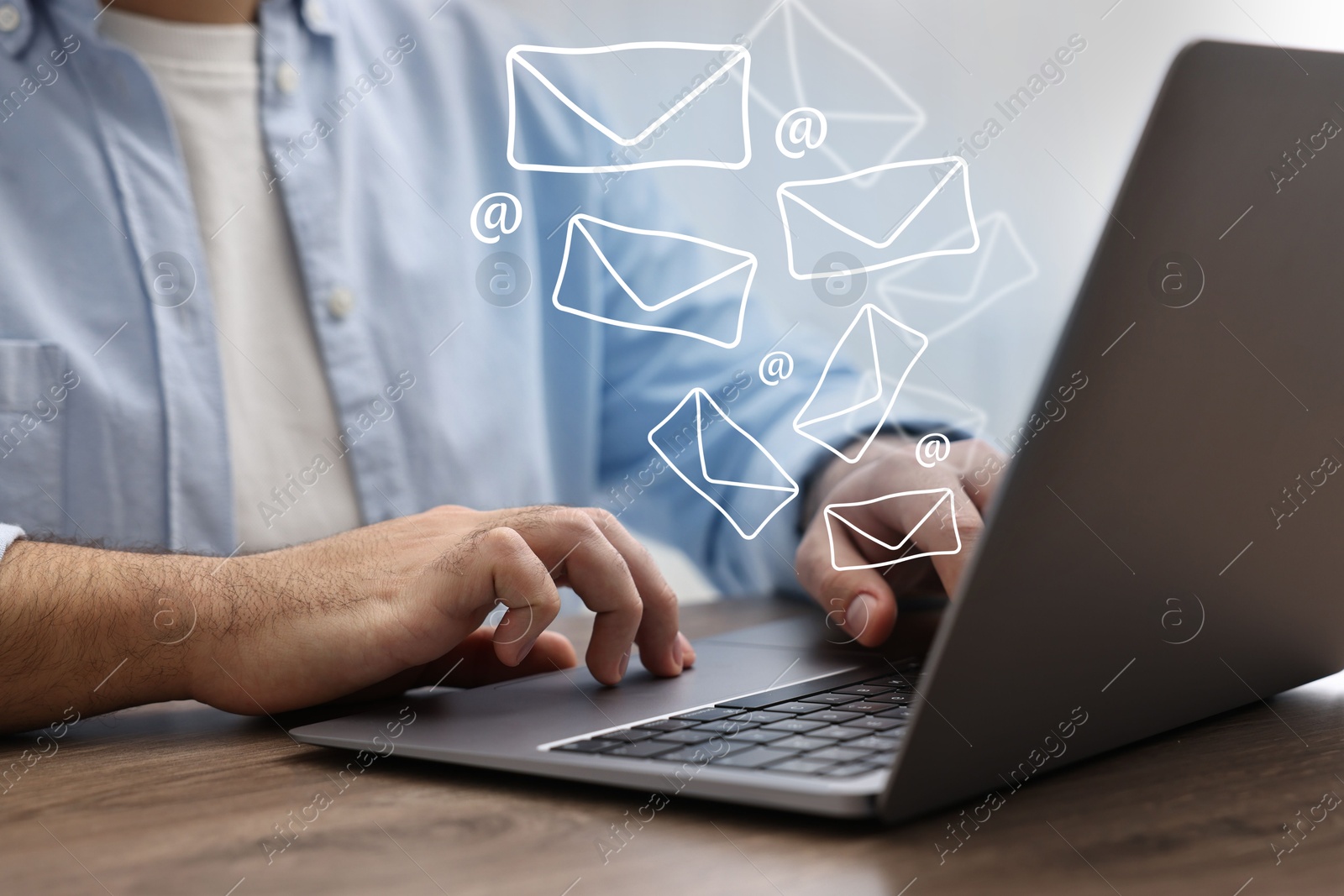 Image of Man using laptop at table, closeup. E-mail address signs and envelopes over computer